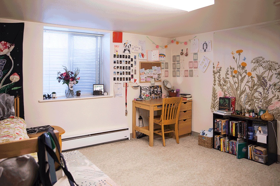 An attractively decorated bedroom with a desk, bookshelf, twin bed and baseboard heater.